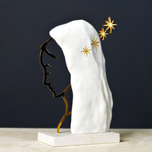Uma figura delicada emerge da junção harmoniosa entre silhueta, manto e estrelas, evocando a presença serena de um ser angélico. A combinação de branco e dourado confere à peça uma leitura luminosa e contemplativa, onde cada material contribui para a sua aura sagrada e intemporal. Esta criação do ateliê criativo da Dalmática celebra a forma feminina como símbolo universal de proteção, beleza e transcendência. Materiais: Resina de poliuretano, folha de ouro, gesso, latão.